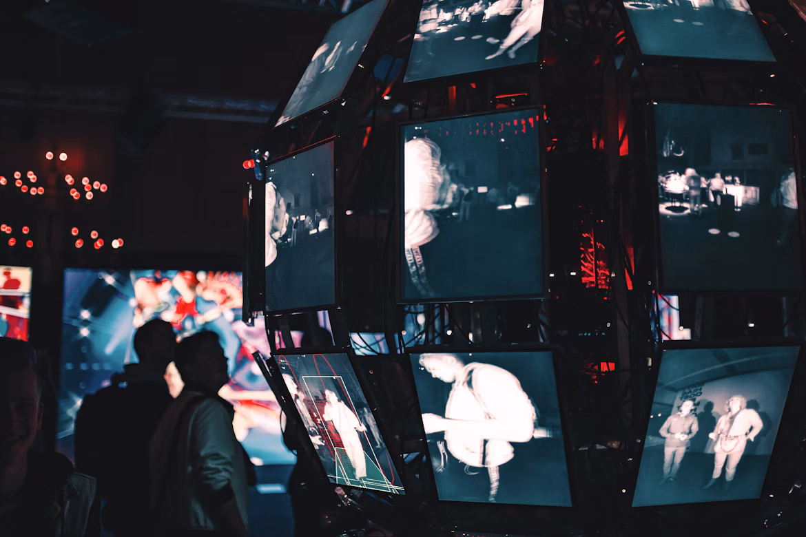 People observing a digital art installation with multiple illuminated screens in a dark room, symbolizing technology, innovation, and modern influence.